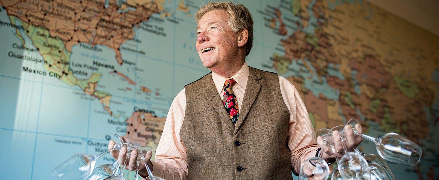 Jackson Lamb holding wine glasses in front of a map of the world