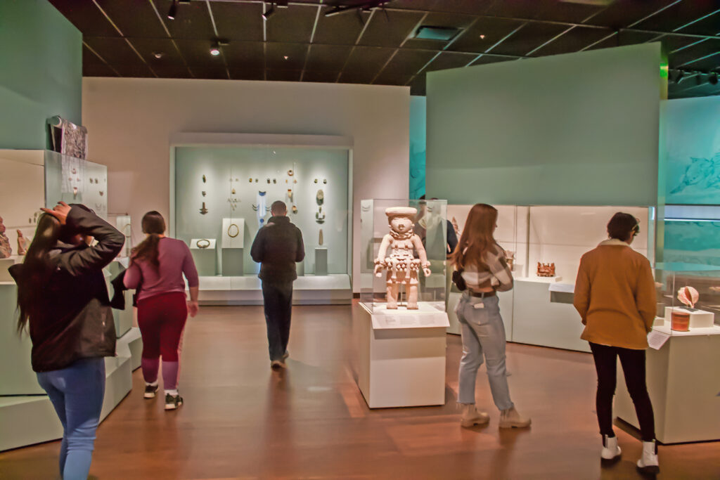 Students wander and observe ancient artifacts in a gallery.