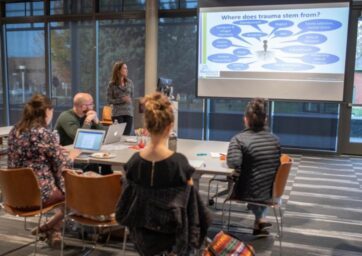 Students and faculty talking in front of a powerpoint screen