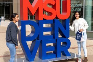 Two students standing next to a big "MSU DENVER" sign outside of the Jordan Student Success Building.