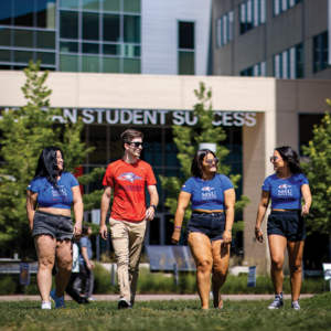 Four students walking on the lawn in front of the Jordan Student Success Building