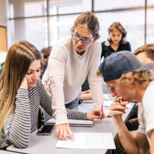 A teacher pointing at a piece of paper talking to two students