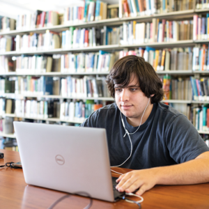 A student sitting in a library working on a laptop