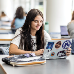 A student sitting at a table looking at a laptop