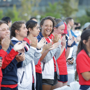 A group of student athletes smiling and clapping at a rally