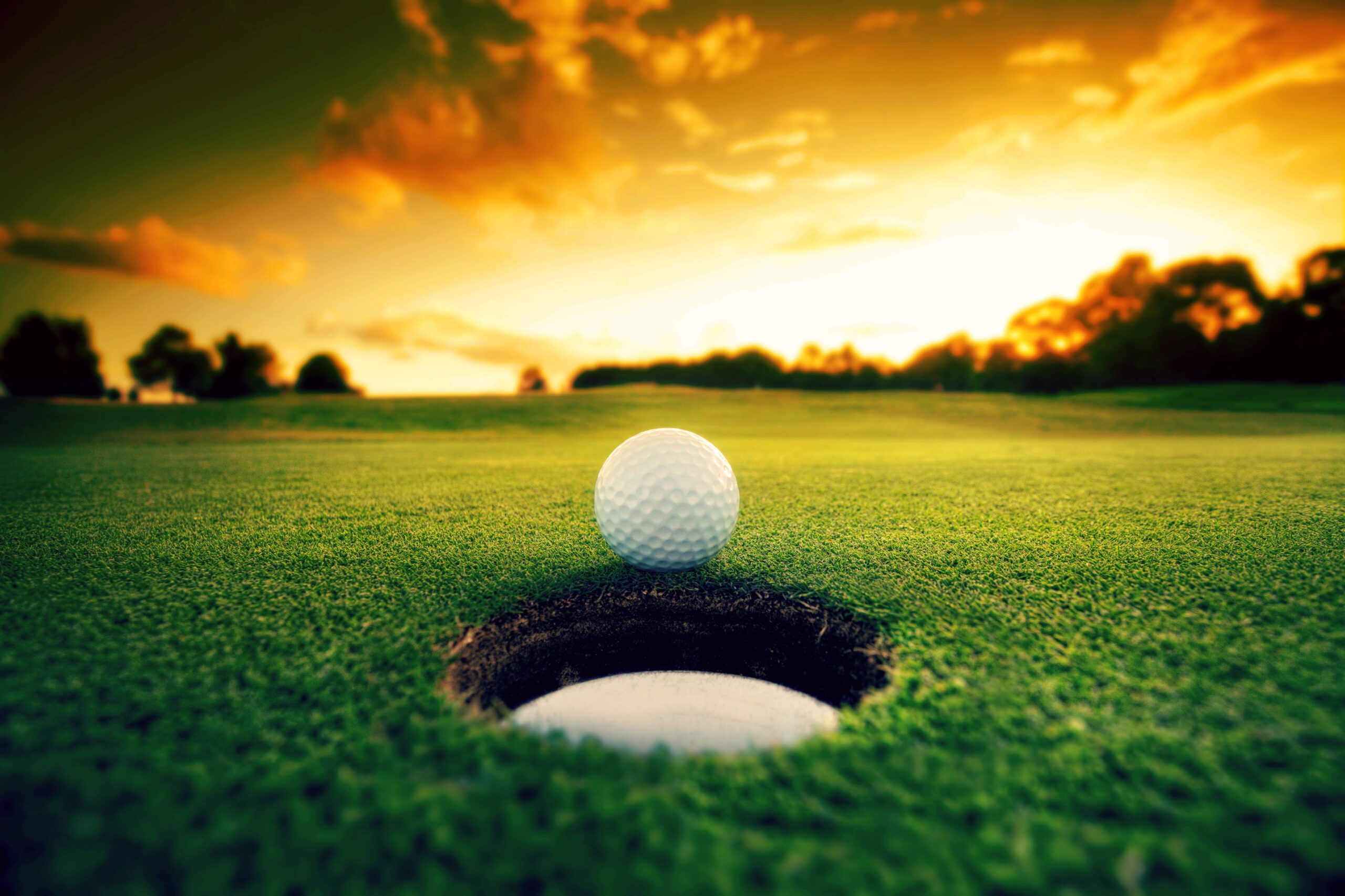 golf ball in front of a hole at sunset
