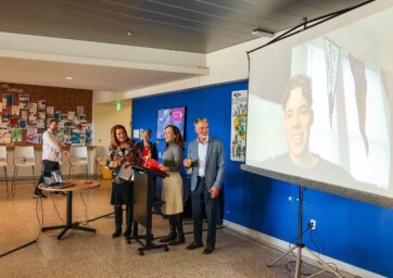 Christy and Ferd Belz standing in front of a projector screen with their son calling in from his classes in Indiana.