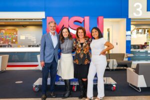 Ferd Belz, President Janine Davidson, Christy Belz, and Mariana Pascual-Miranda standing in front of the red and blue MSU Denver sign in JSSB.