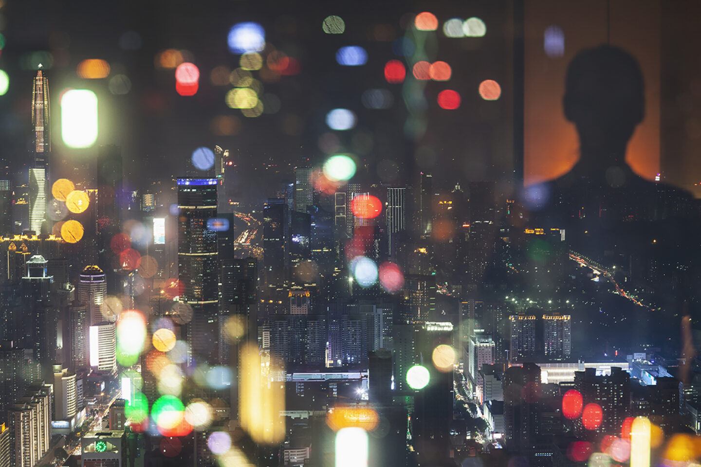 Silhouette looking out window at city lights at night.