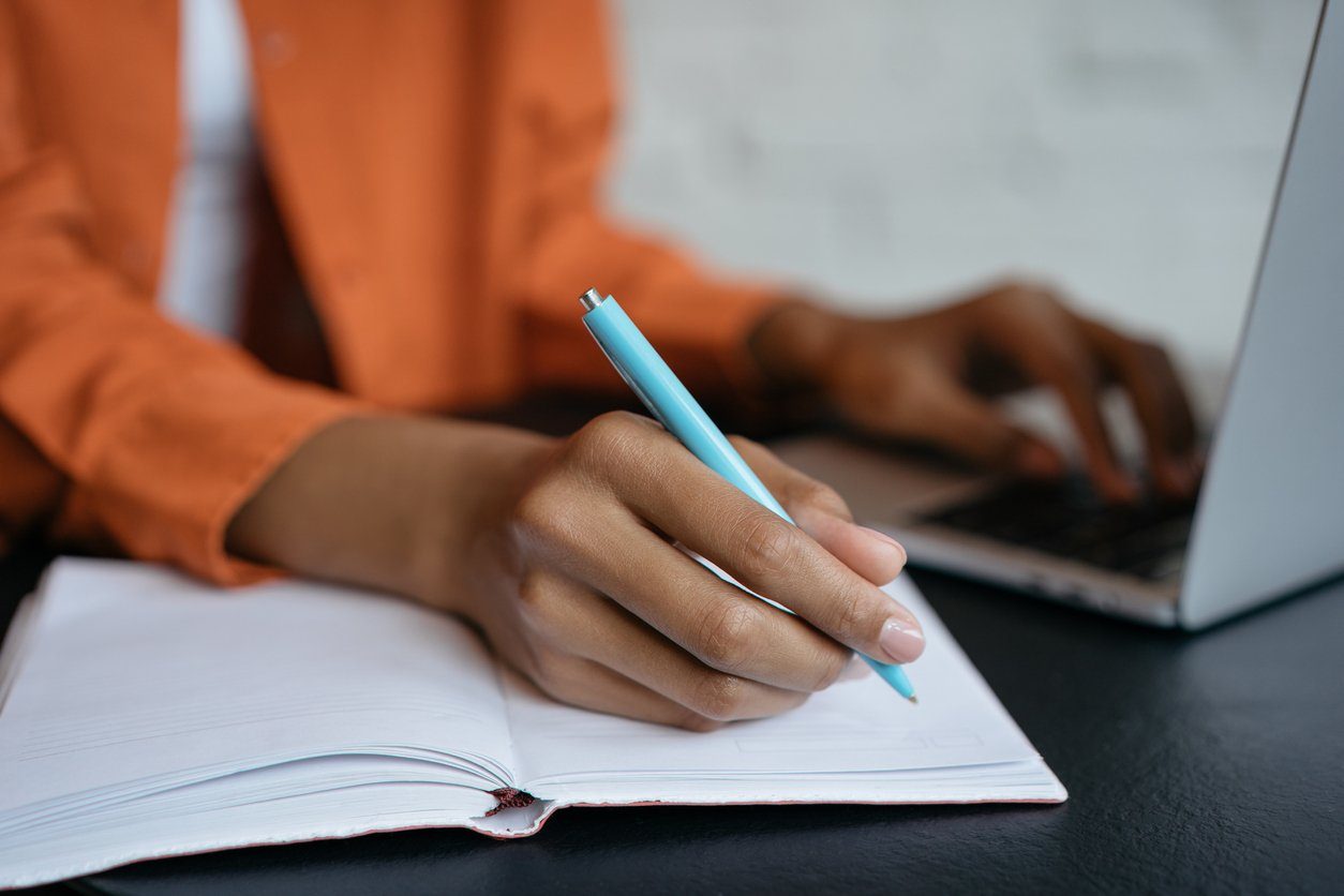 Close-up shot of hand holding pen and writing in notebook, working at home. E-learning