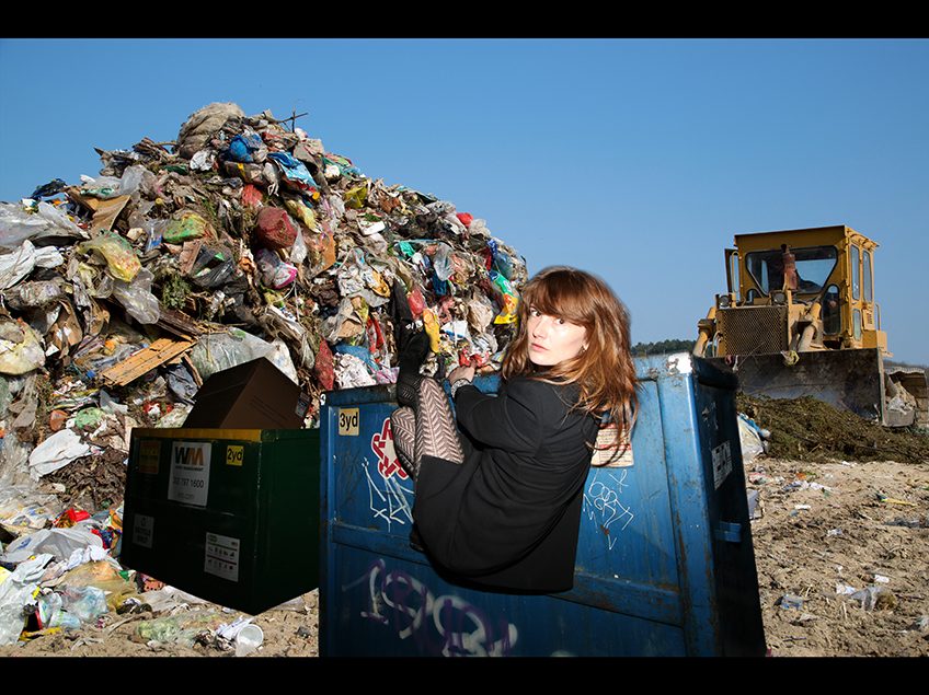 Garbage pile and a woman hanging from a dumpster.