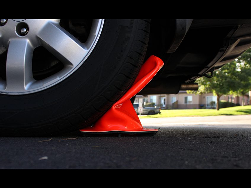 Close up of a car tire crushing an orange traffic cone.