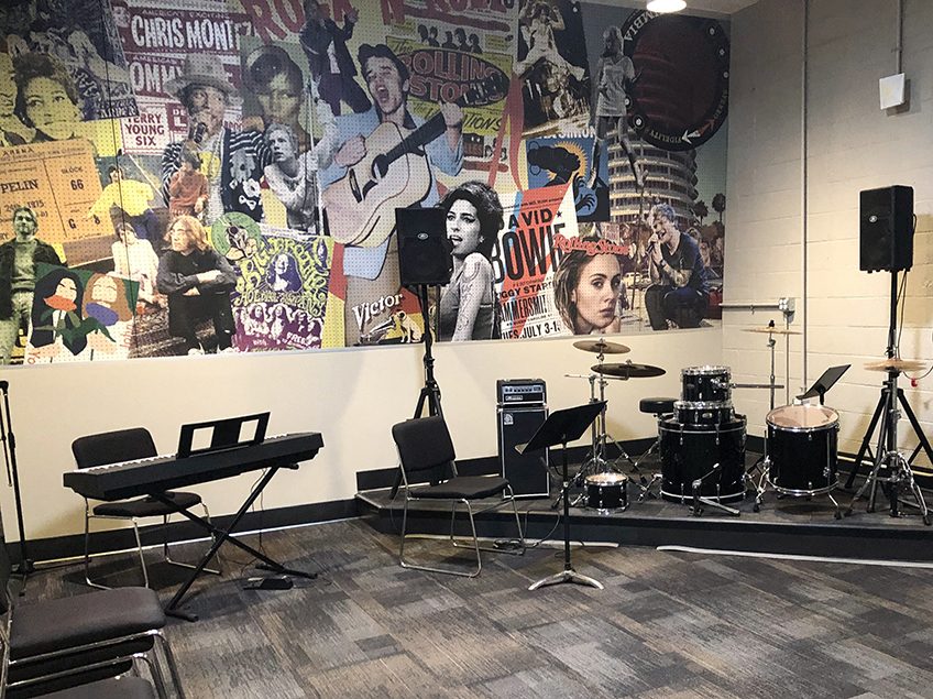 a mural of rock stars in a classroom over a keyboard and drumset and guitars