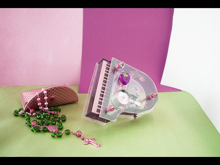Pastel colored still life with toy piano, beads, and small gold clutch.