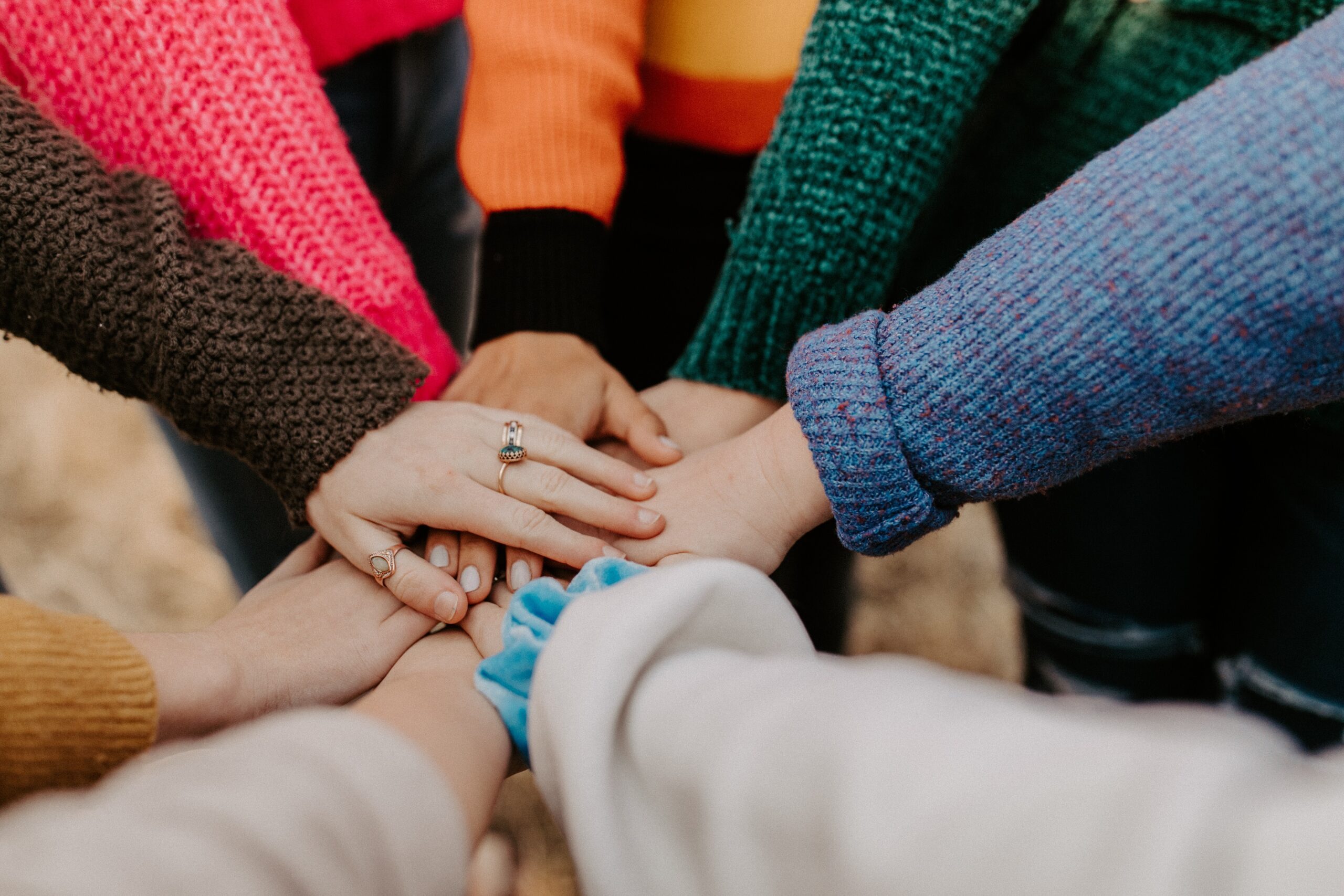 Several people with different colored long sleeves placing their hands on top of each other