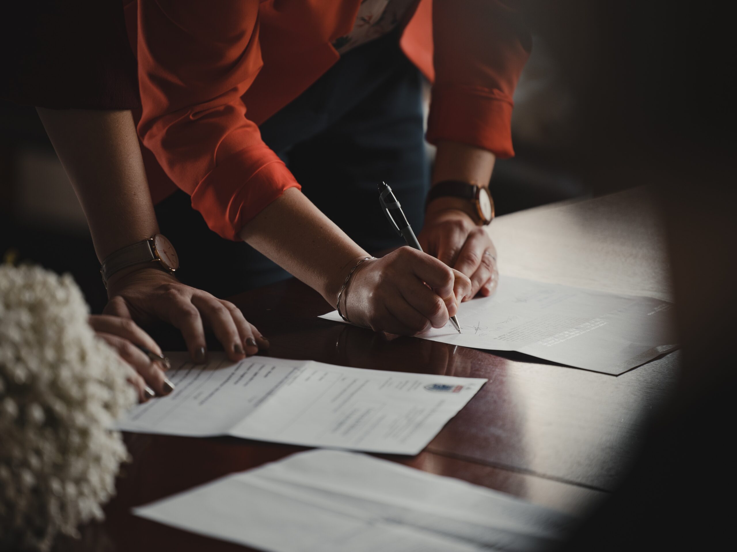 Two sets of hands with pieces of paper on a table, one person is signing one of the pieces of paper