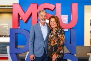 Ferd and Christy Belz standing in front of the red and blue MSU Denver sign