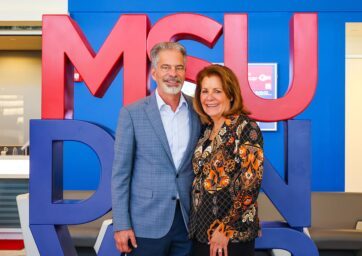 Ferd and Christy Belz standing in front of the red and blue MSU Denver sign