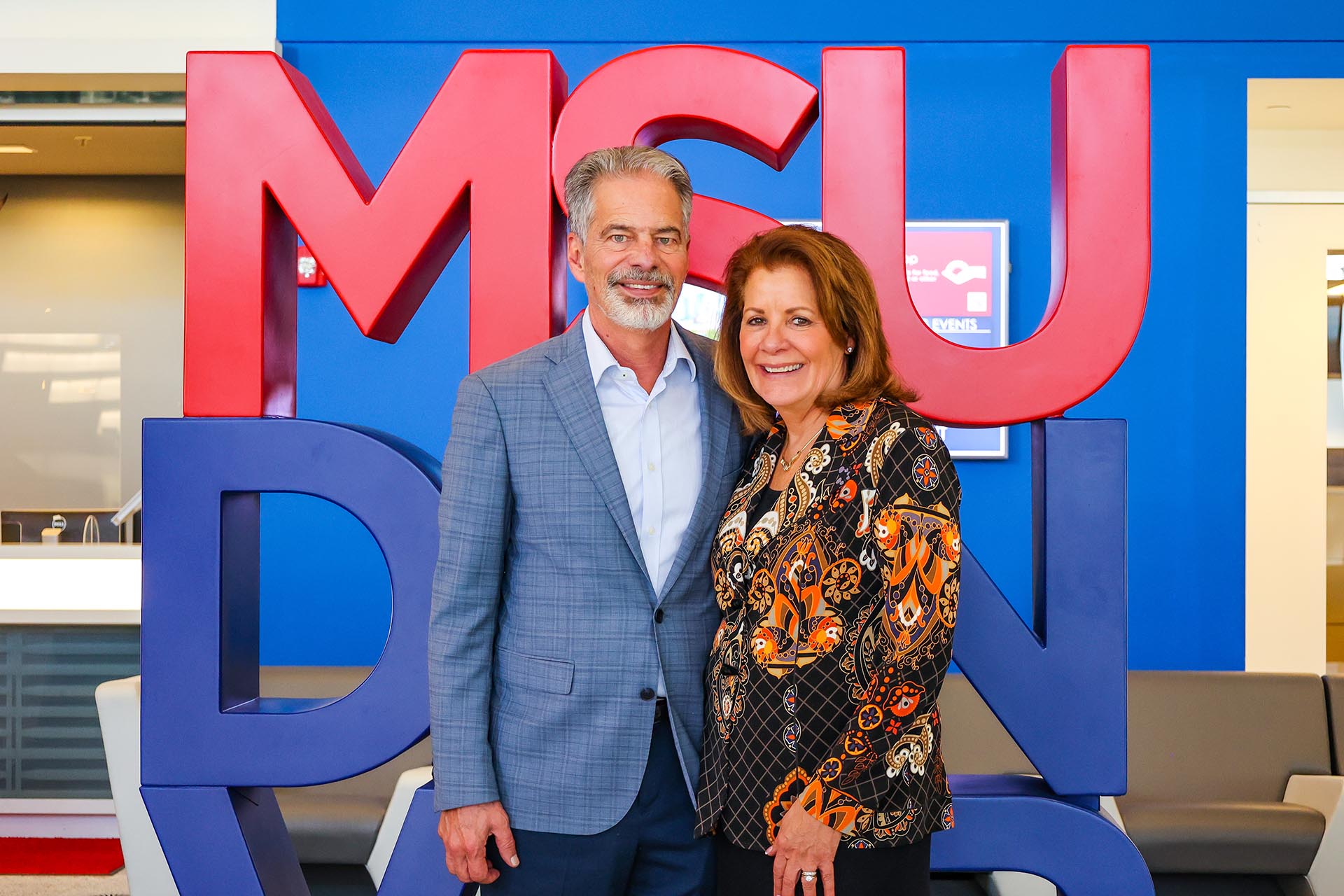 Ferd and Christy Belz standing in front of the red and blue MSU Denver sign