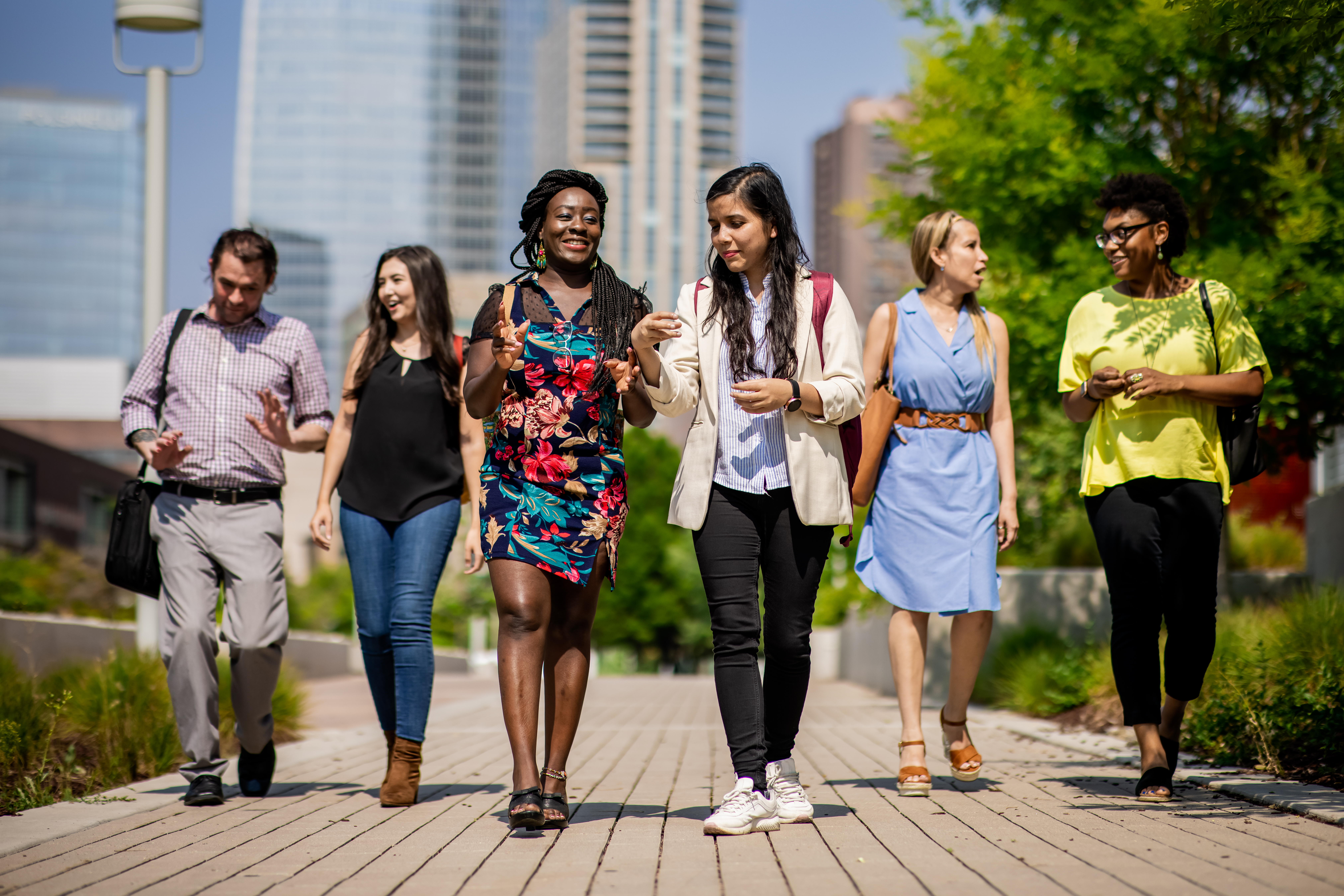 Image of 6 students walking toward the camera, chatting with each other, on a bright, sunny day outside on Auraria Campus.