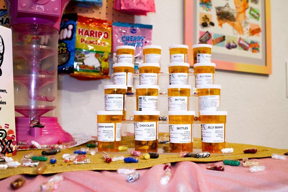 Alexcia Pickrell, Sickly Sweet, 2022, mixed media of diplay of pill bottles and pills on a pink tablecloth