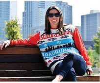 Woman sitting on a bench on campus wearing a Roadrunners sweater with downtown in the background