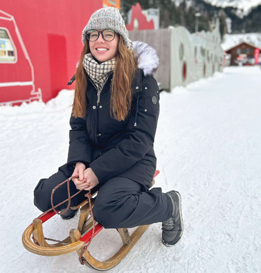 A student sitting on an old wooden sled in the snow.