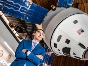 MSU Denver junior Brian Ysasaga, an Aerospace Systems Engineering Technology major, stands with arms crossed in front of the Orion space capsule replication hanging in the AES building.