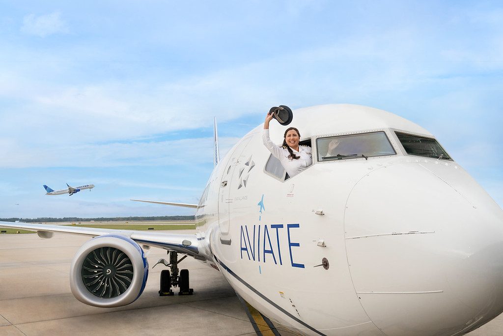 A pilot waving her hat outside the front flight deck window of a B-737 aircraft.