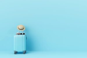 Blue suitcase with sun glasses, hat and camera on pastel blue background.