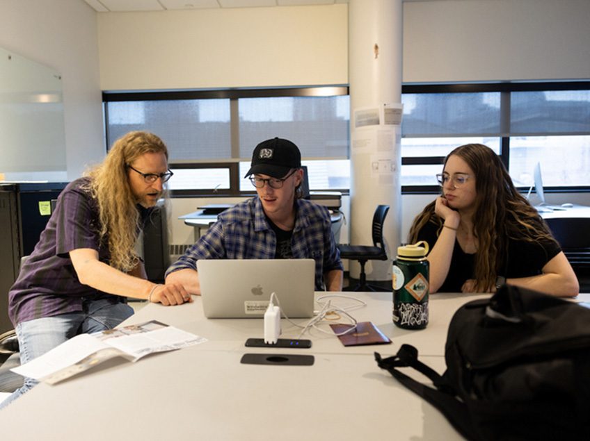 Professor Bergman works with students on a Macbook pro.