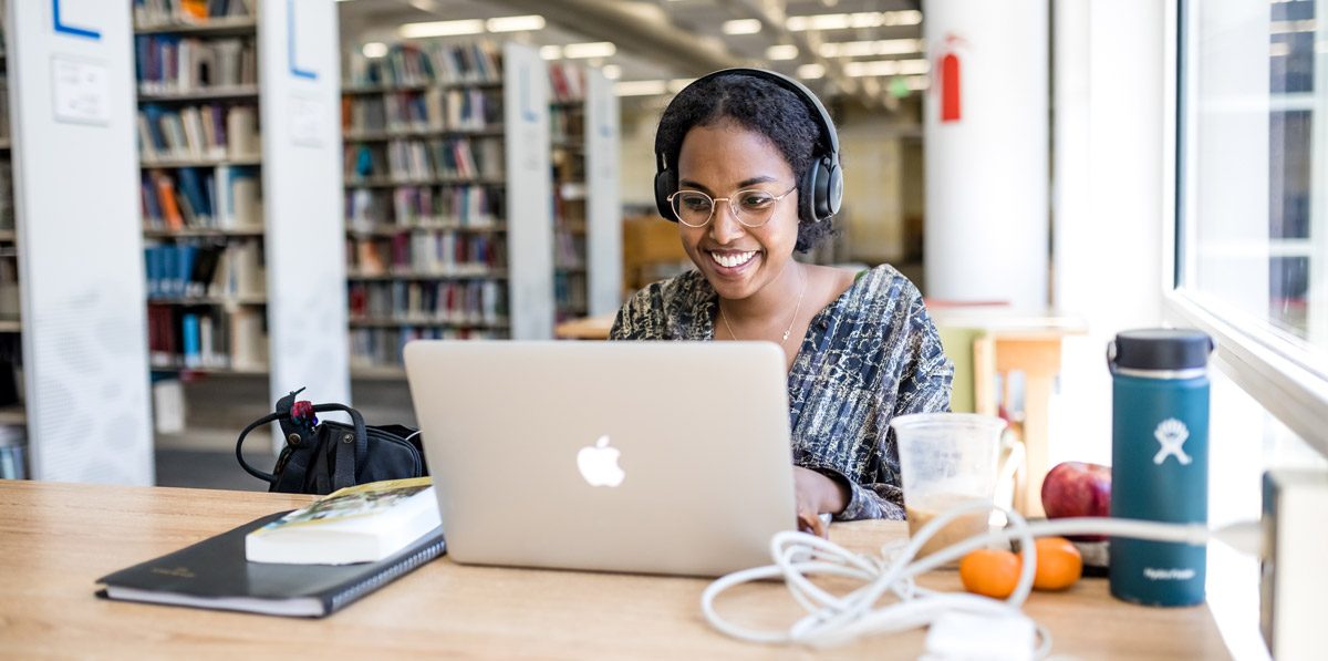 Smiling female student on a MacBook in a library