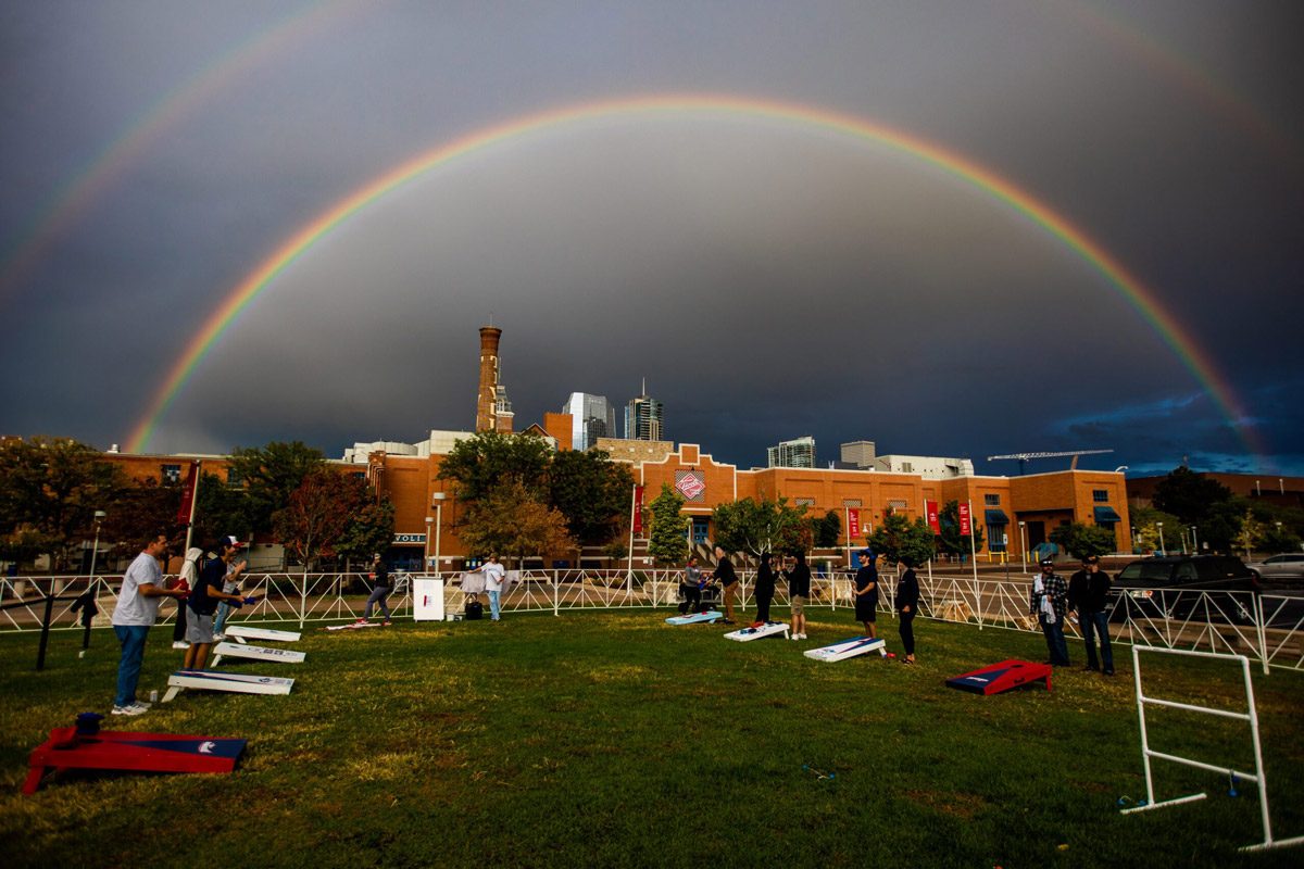 A group of people playing cornhole in front of the Tivoli with a storm and rainbow in the background above the Tivoli