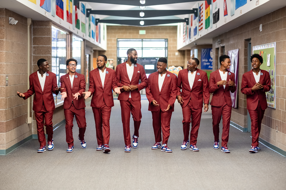 Decorative: Photo of the MiSTERs walking through a school hallway in matching red suits and sneakers.