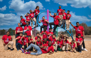 A photo of one of the MSU Denver MISTERs sitting with a group of young students and holding two books.