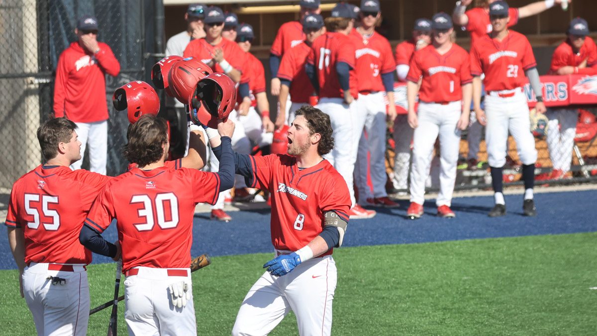 Three baseball players slapping helmets with Zach Schuler at home plate after a home run in February 2023