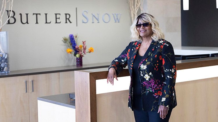 Dawn Bookhardt standing at a desk at Butler Snow with flowers on a shelf behind her.