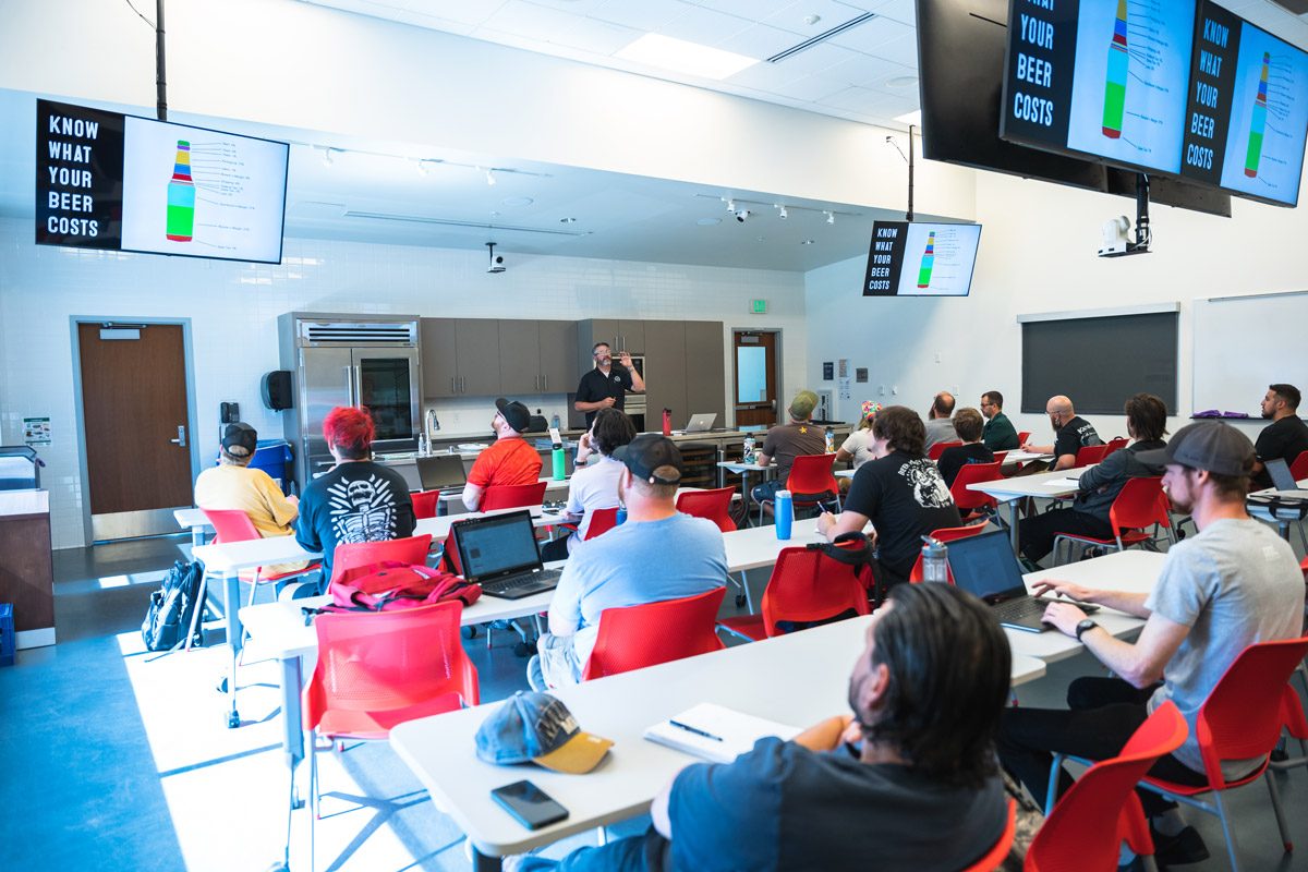 A bright classroom full of students with a professor in front of the room