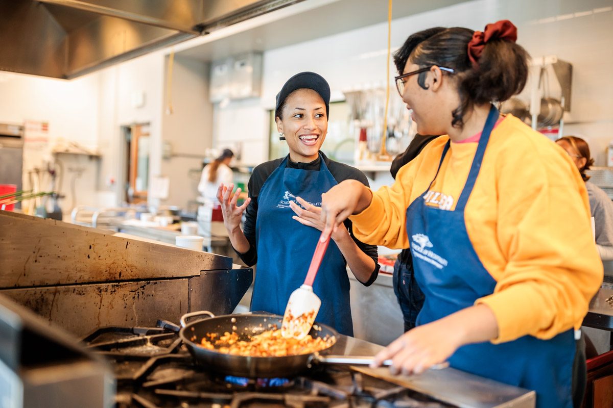 Two smiling female students cooking in a pan