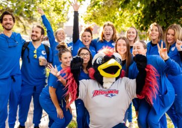 Healthcare students in royal blue scrubs posing for a picture with Rowdy on a sunny, fall day
