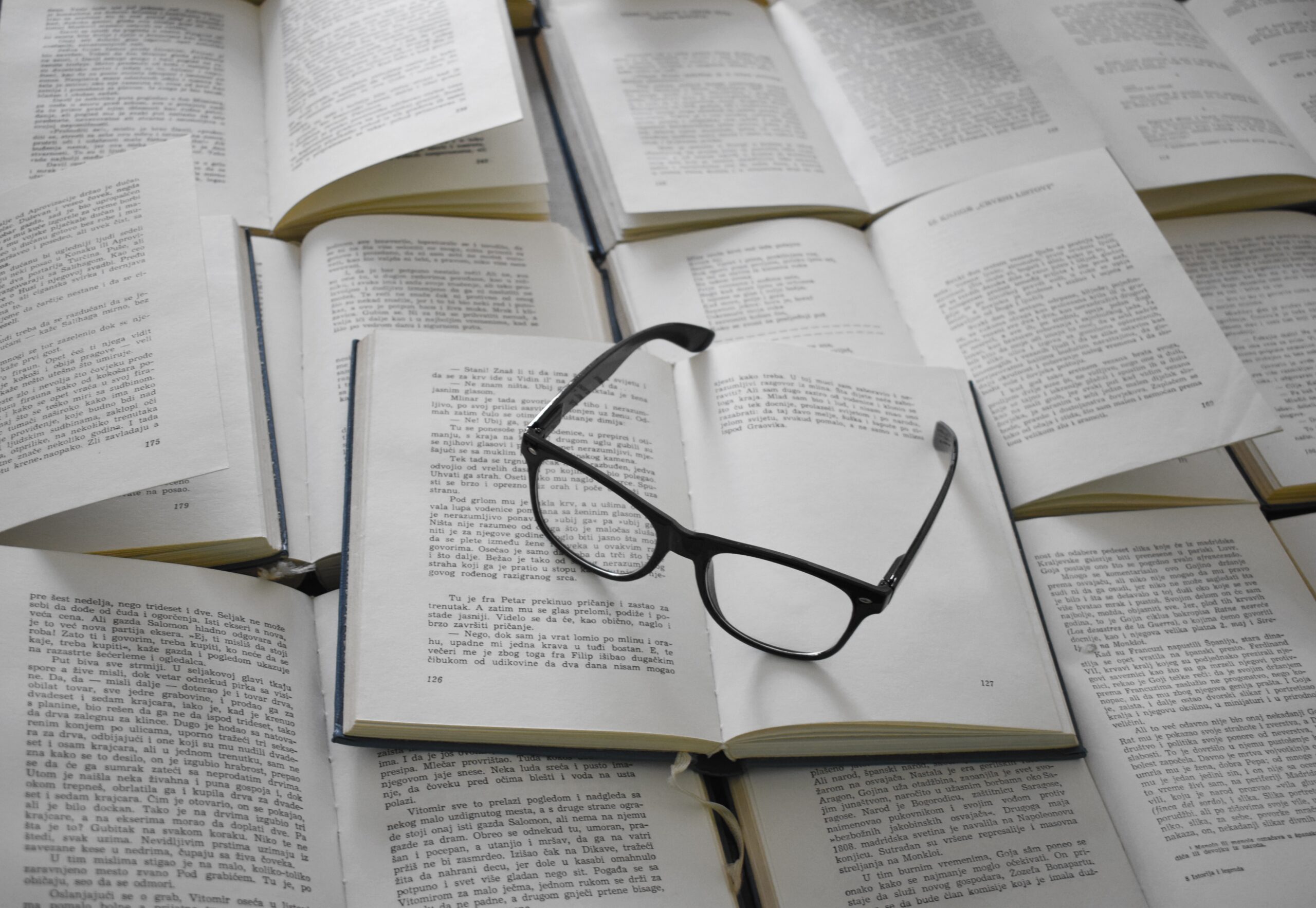 A pair of eyeglasses on top of an open book, which is on top of several books as the base.