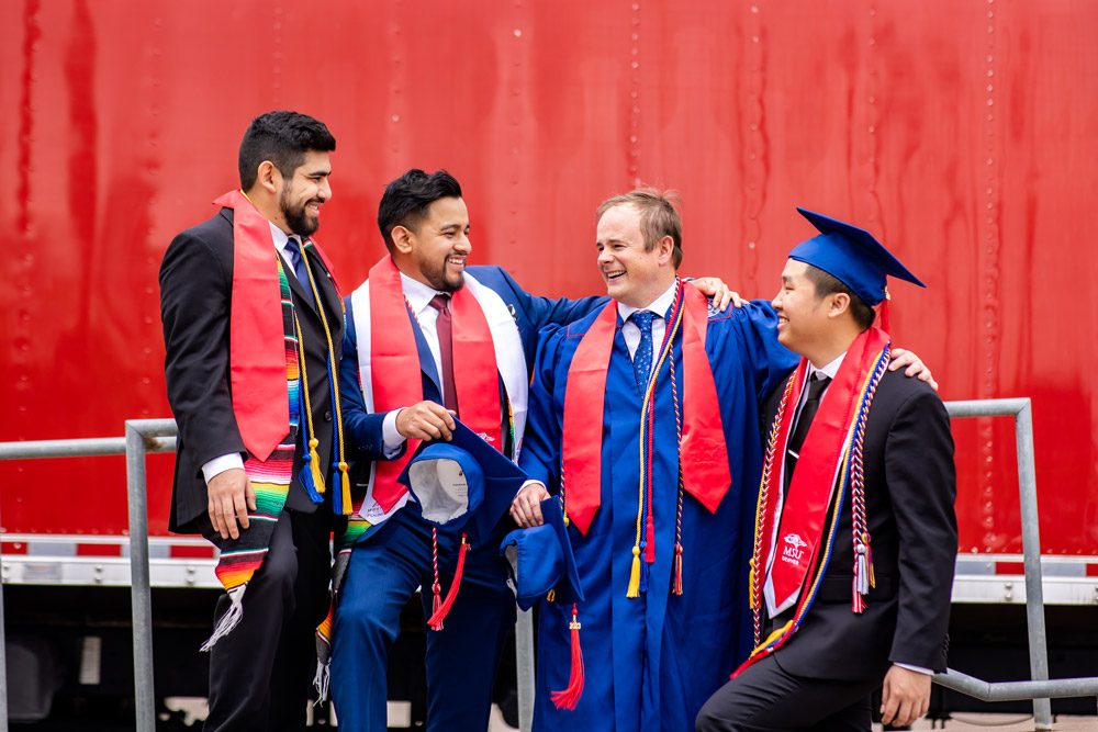 A group of four male graduates smiling and laughing at commencement in May 2023
