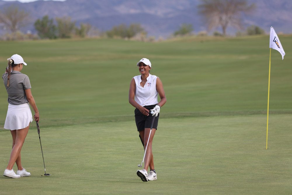 An MSU Denver women's golf athlete smiling as she walks off a green.
