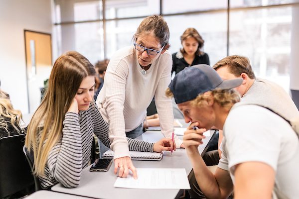Professor helping several students in a brightly lit classroom.
