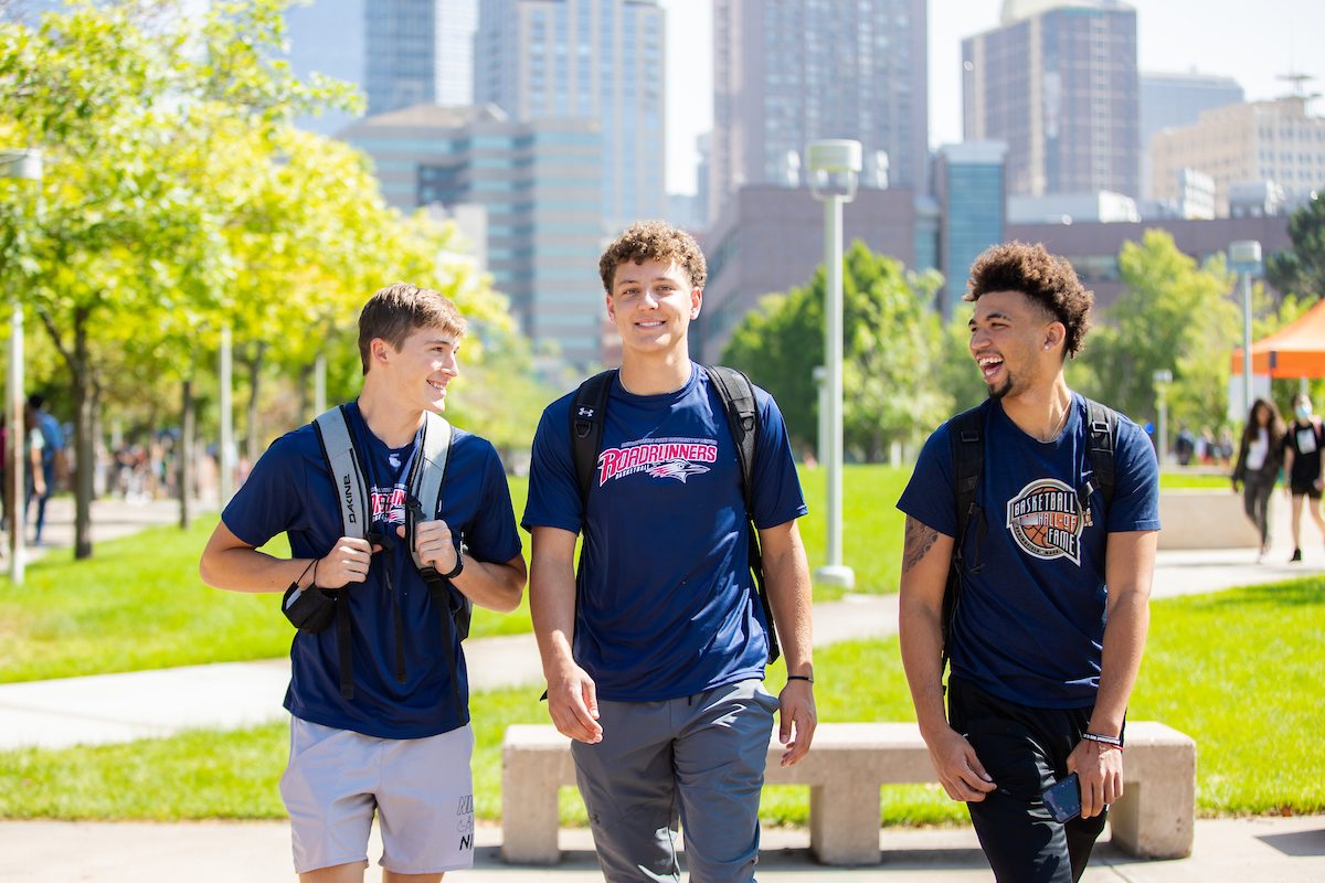 Three students standing together in front of greenery and the Denver skyline.