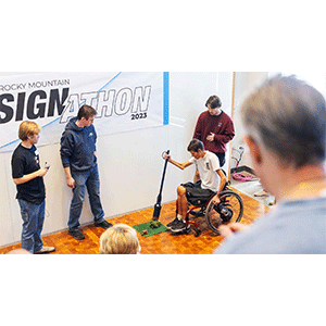 Person in wheel chair using a prototype pooper-scooper while audience watches