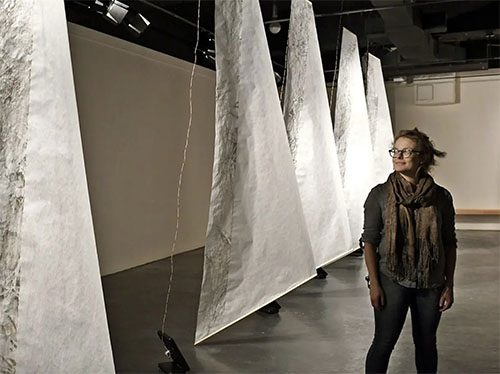 Professor Anne Yoncha in the gallery with large fabric sails behind.