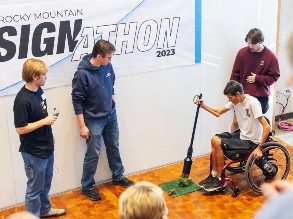 MSU Denver industrial design students look on as a person in a wheelchair uses their prototype to demonstrate picking up pet waste.