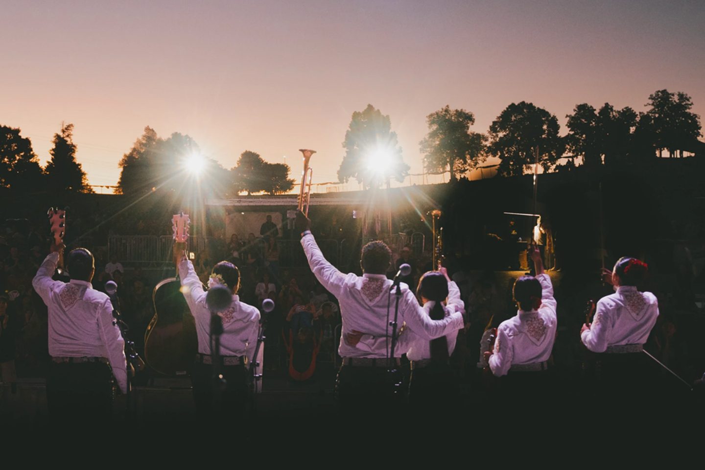 Mariachi group on stage waving to audience at outdoor concert