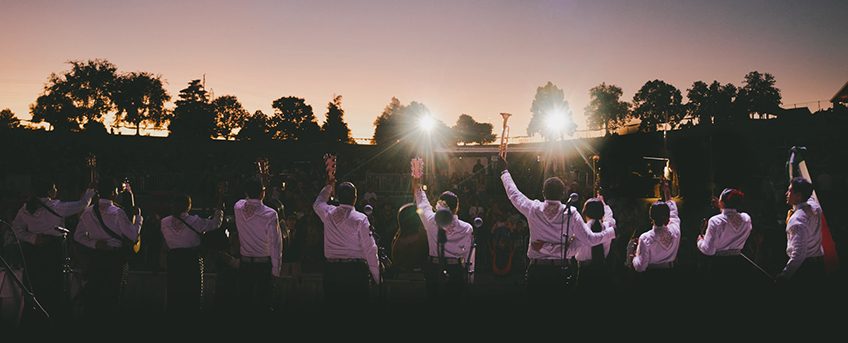 Mariachi group on stage waving to audience outdoors